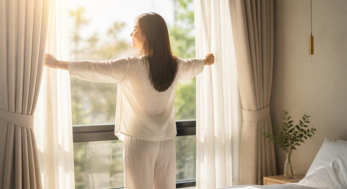 朝のカーテンを開け生活を取り戻す女性